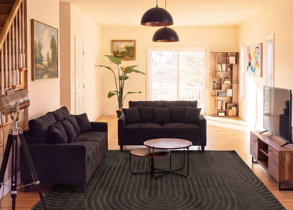 Salon moderne avec deux canap&eacute;s fonc&eacute;s, des tables basses gigognes, un meuble TV et un grand tapis dans un espace lumineux.